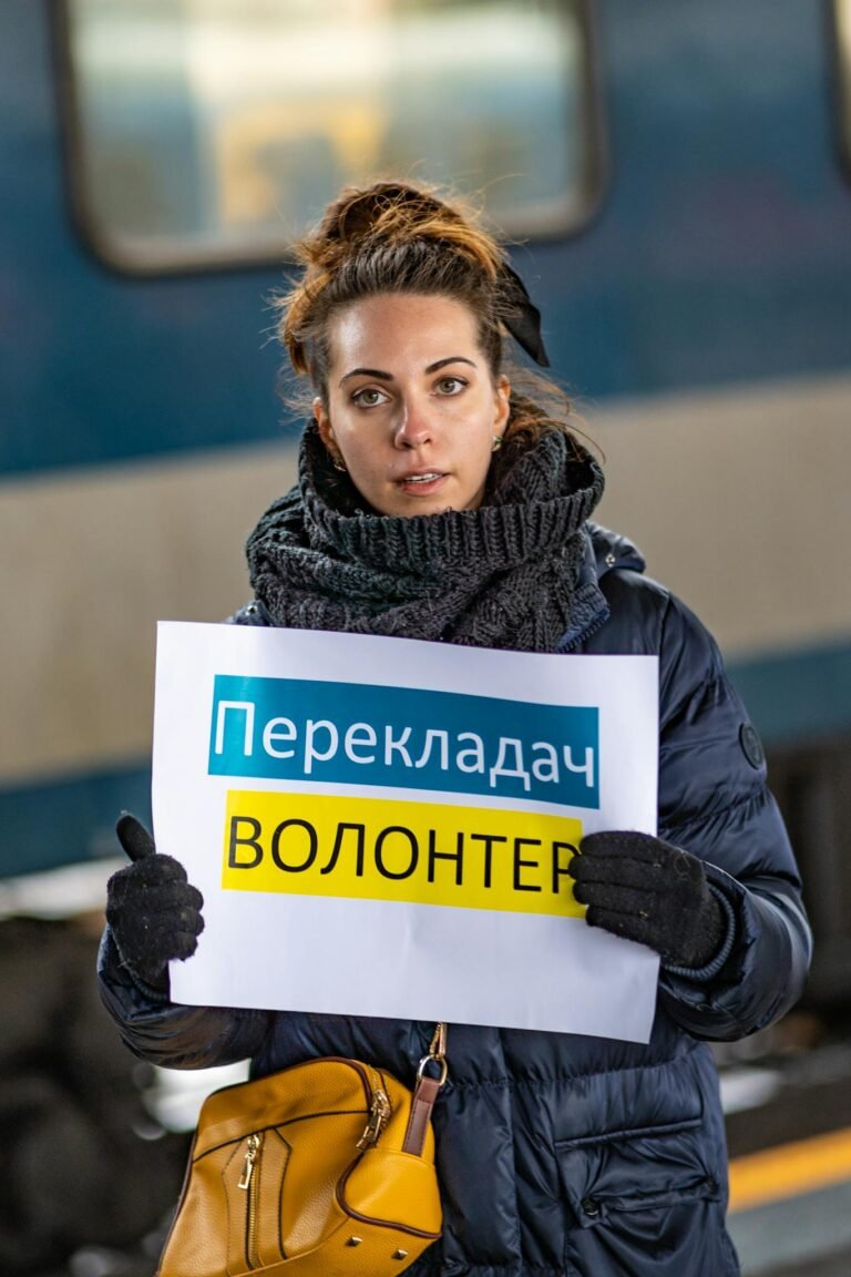 A woman in winter clothing holds a volunteer sign at a train station in Budapest, Hungary.