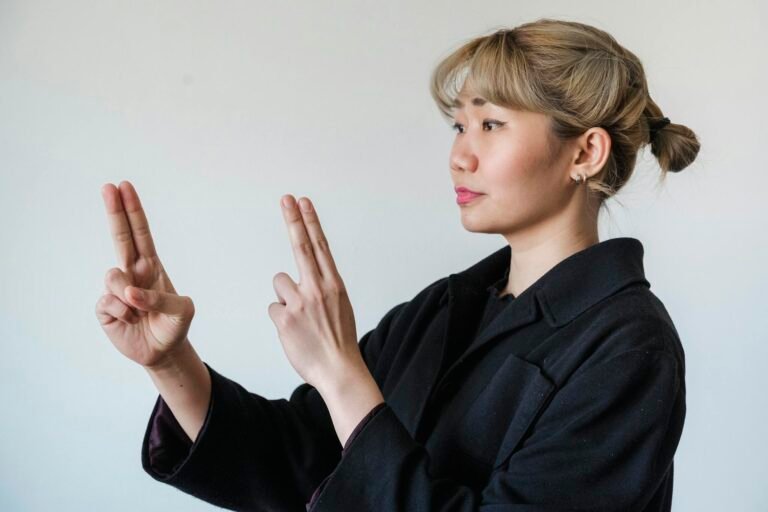 Asian woman gesturing with hands, demonstrating sign language on a white background.