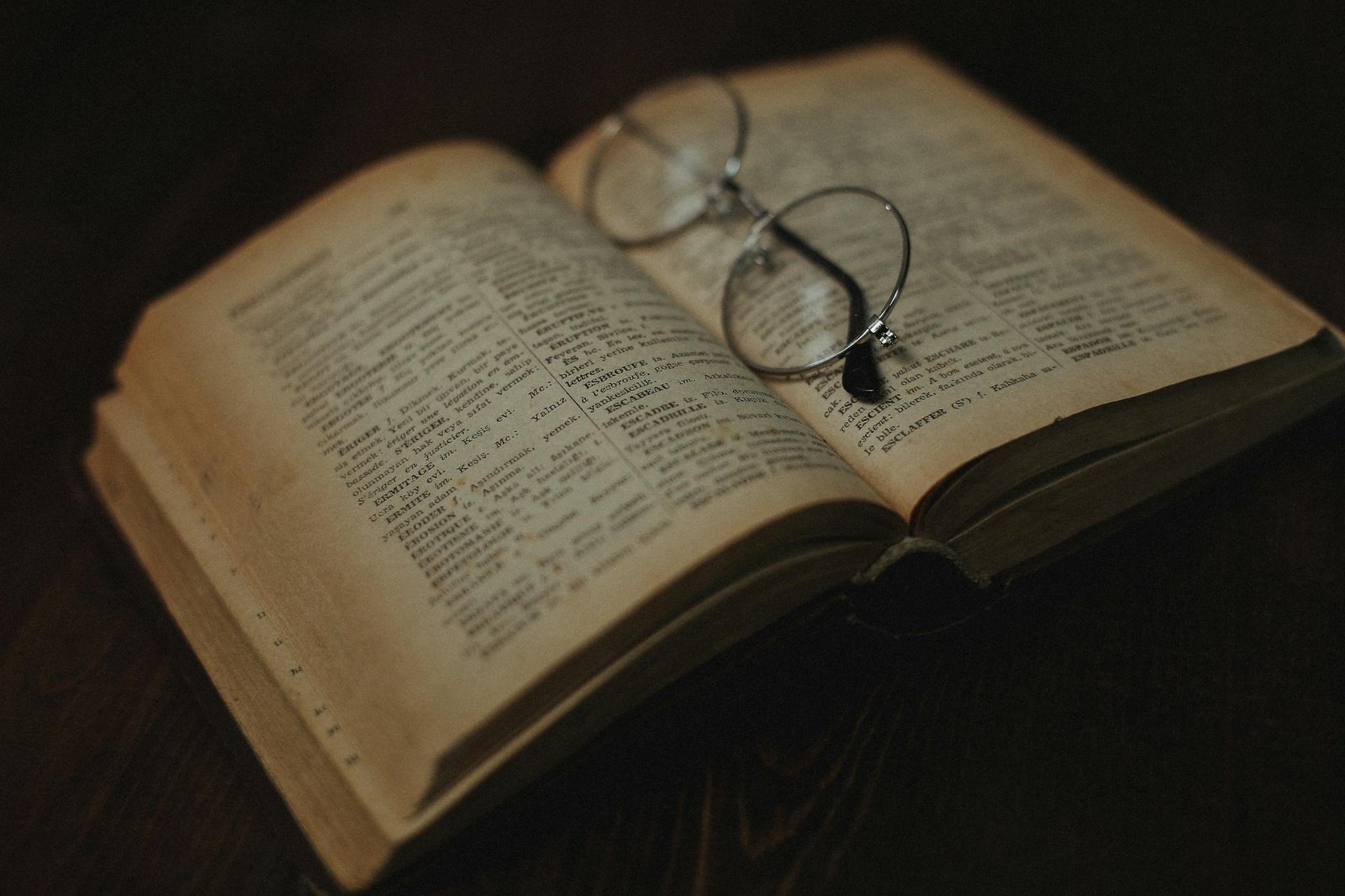 An antique book opened with eyeglasses resting on its pages. Aesthetic, warm lighting.